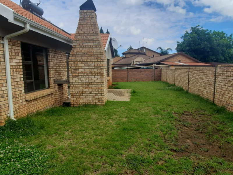 A rear exterior view of a townhouse featuring a brick facade, a built-in brick chimney, and a private garden area enclosed by brick boundary walls.