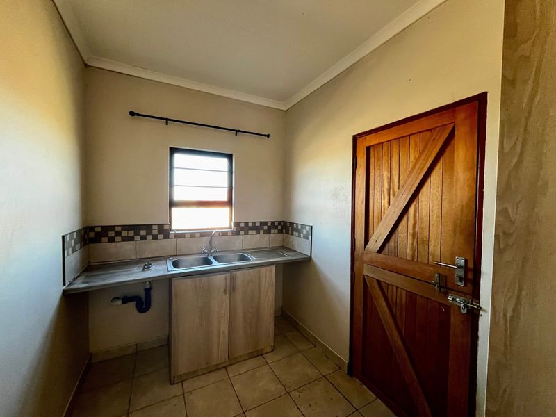 A functional laundry area featuring a stainless steel sink, tiled splashback, and a solid timber door, providing a practical utility space.