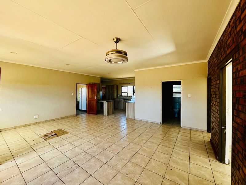 Spacious open-plan living area featuring tiled floors, an exposed brick feature wall, and an adjoining kitchen space with built-in cabinetry.