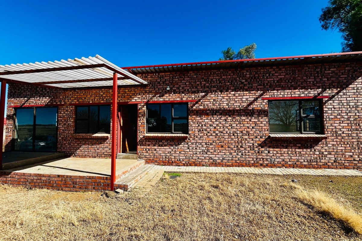 Rear exterior view of a townhouse featuring exposed brickwork, a covered patio area with a pergola, and aluminum-framed windows.