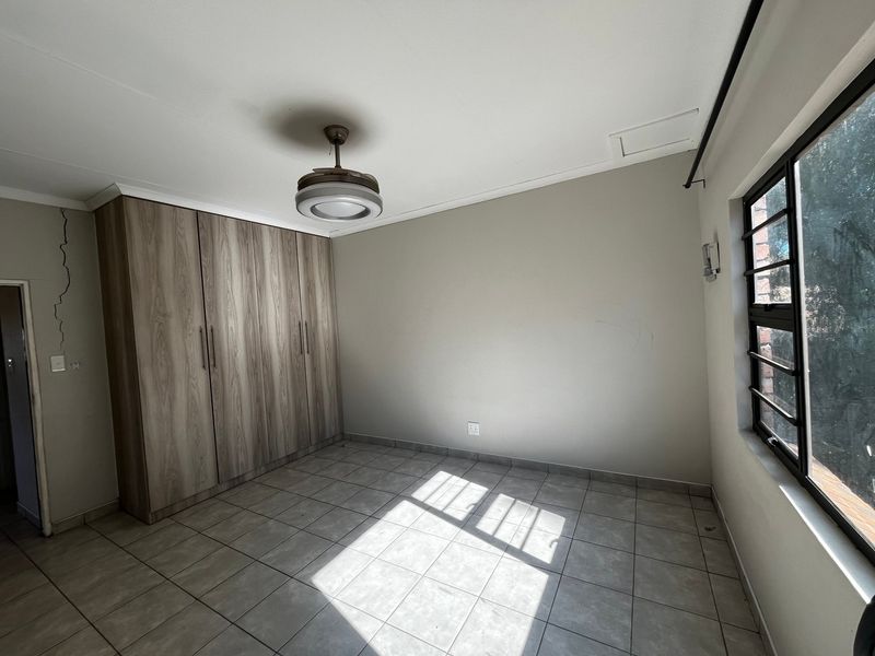 An empty bedroom featuring tiled flooring, built-in cupboards, and a ceiling fan, with a visible wall crack requiring attention.