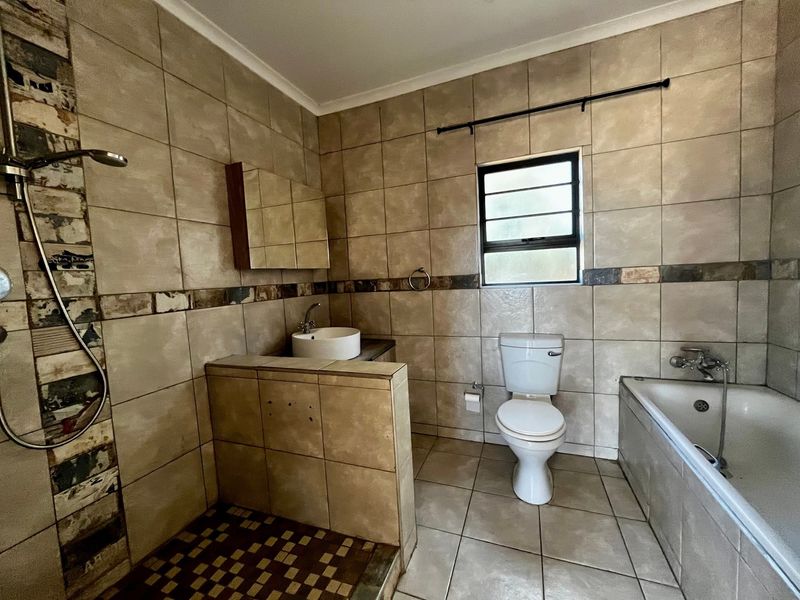 A dated bathroom featuring a shower, bathtub, toilet, and basin with tiled finishes, requiring some maintenance and cosmetic updates.