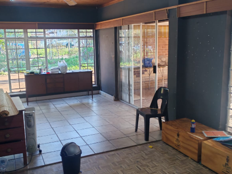 Spacious living area featuring a timber ceiling, ceiling fan, and a combination of tiled and parquet flooring with large windows and sliding door access.