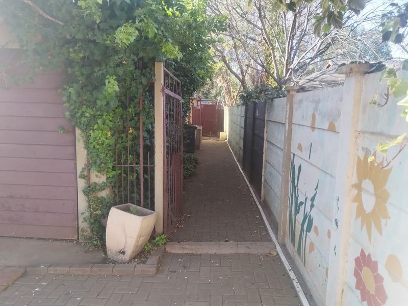 A narrow paved side walkway leading to the rear of the property, enclosed by a precast concrete boundary wall and metal gate.