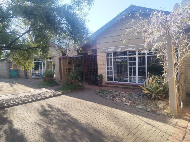 Front elevation of a residential property featuring a paved driveway, face brick facade, and timber cladding with security gates and multi-pane windows.