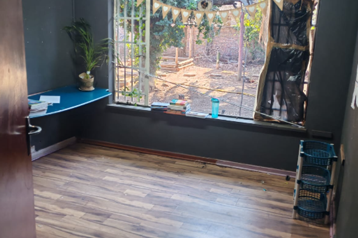 A bedroom featuring laminate flooring, a ceiling fan, and a built-in desk, with a large window overlooking the rear garden area.