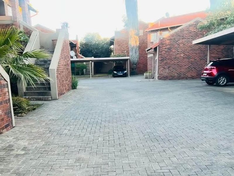 Exterior view of an apartment complex featuring a paved driveway, brick building facades, and covered carport parking spaces.