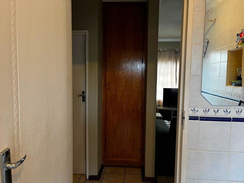 A functional hallway featuring tiled flooring and a built-in wooden cupboard, providing access to adjacent living areas and rooms.