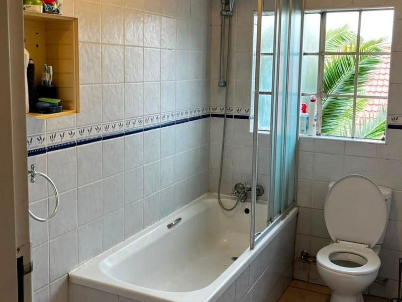 A functional bathroom featuring a bathtub with a shower screen, toilet, and tiled walls with a decorative border.