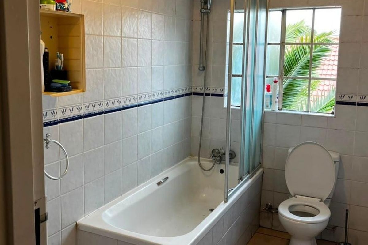A functional bathroom featuring a bathtub with a shower screen, toilet, and tiled walls with a decorative border.