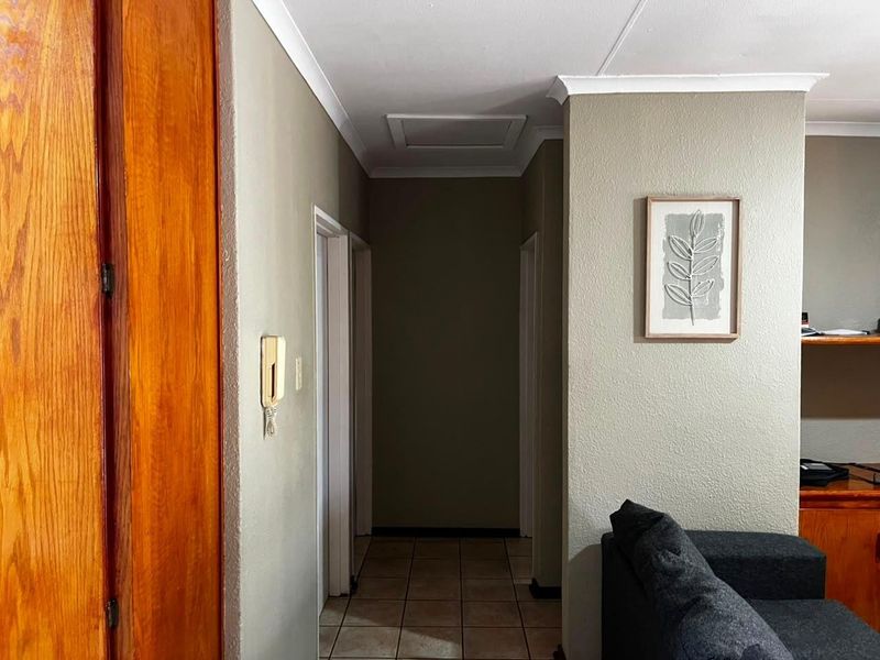 A functional hallway featuring tiled flooring, coved cornicing, and a wall-mounted intercom system, providing access to various rooms within the apartment.