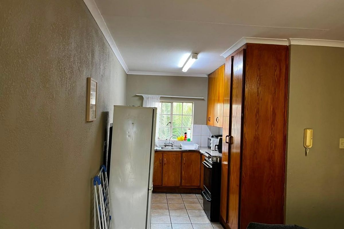 A functional kitchen featuring wooden cabinetry, tiled flooring, and a stainless steel sink, offering a practical layout with potential for modern updates.