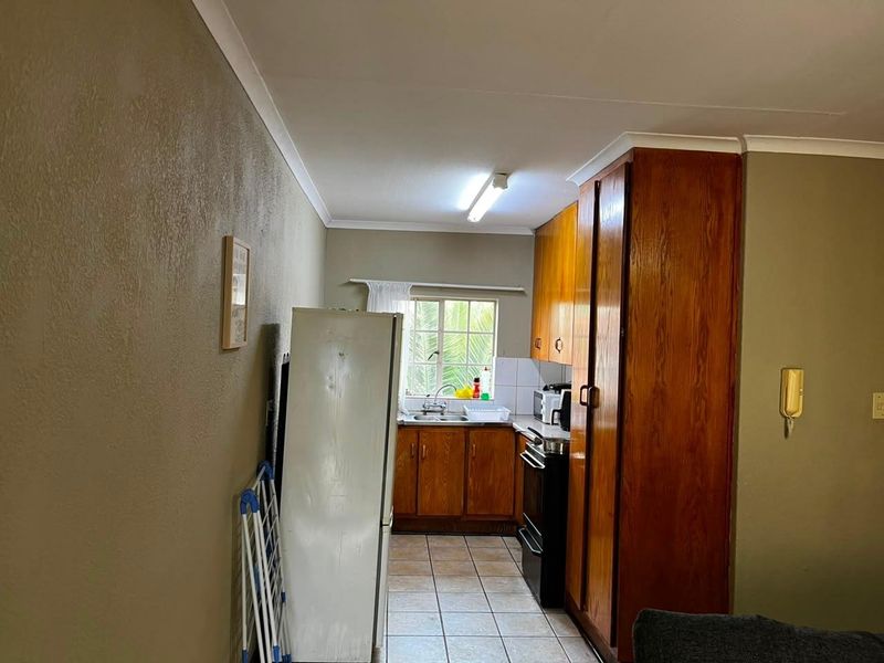 A functional kitchen featuring wooden cabinetry, tiled flooring, and a stainless steel sink, offering a practical layout with potential for modern updates.
