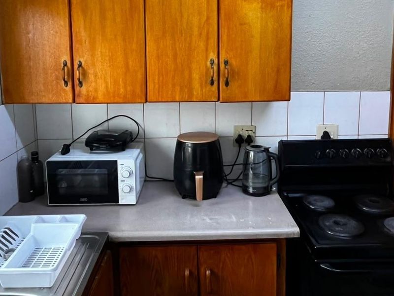 A compact kitchen featuring wooden cabinetry, tiled backsplash, and a freestanding electric stove, offering a functional layout with potential for modern updates.