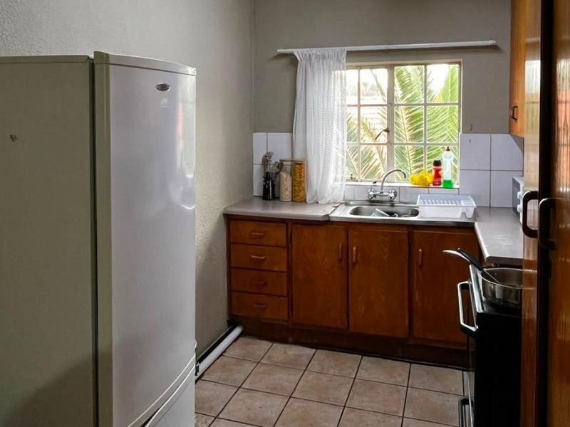 A functional kitchen featuring wooden cabinetry, laminate countertops, a stainless steel sink, and tiled flooring, offering potential for modernization.