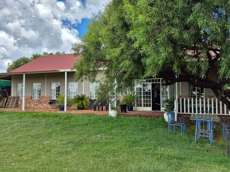 Rear view of the property featuring a covered patio, brick and plaster facade, and a metal roof, set against a spacious garden area.