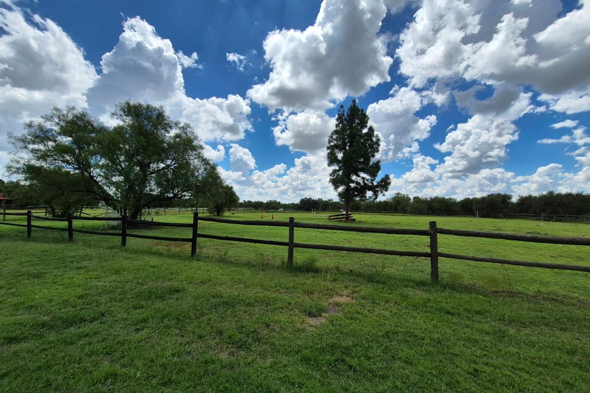 A wide-angle view of a spacious, grassed garden area enclosed by timber post and rail fencing under a bright, cloudy sky.