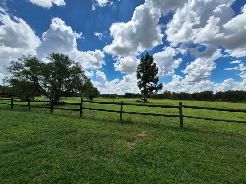 A wide-angle view of a spacious, grassed garden area enclosed by timber post and rail fencing under a bright, cloudy sky.
