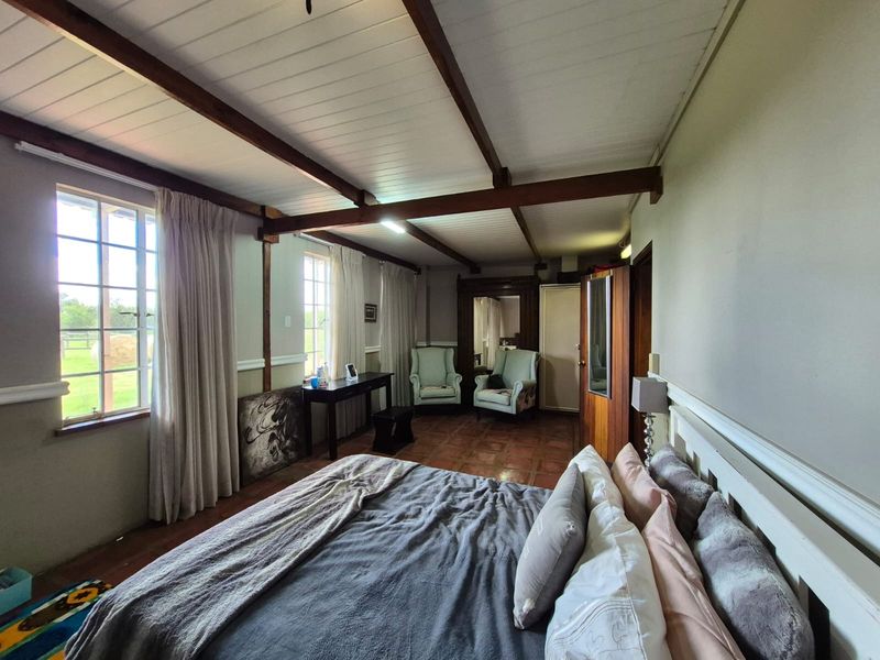 Spacious bedroom featuring exposed timber ceiling beams, terracotta floor tiles, and large windows providing natural light and garden views.