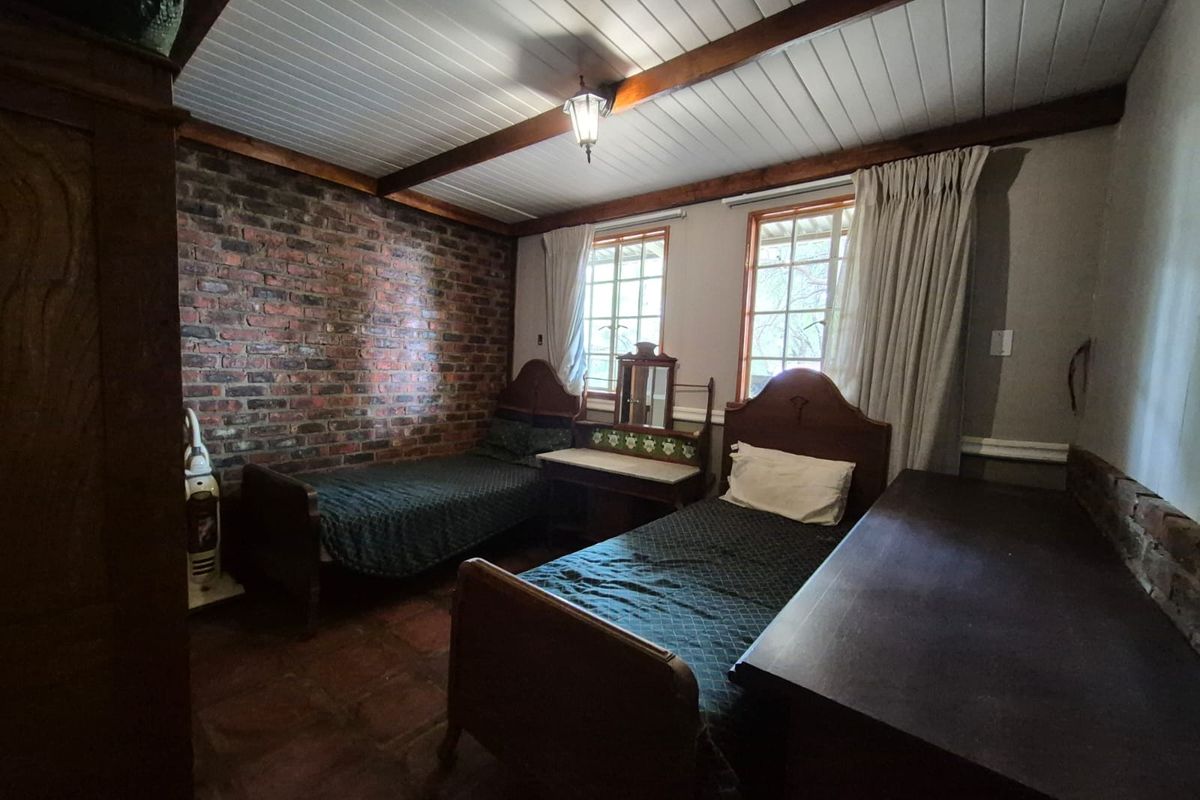 A bedroom featuring exposed brick walls, timber ceiling beams, and tiled flooring, providing a rustic aesthetic with natural light from two windows.