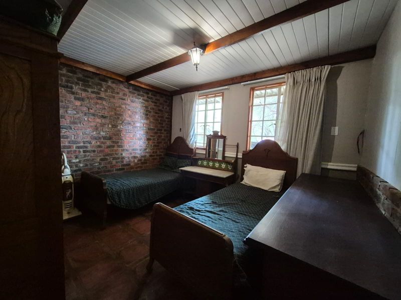 A bedroom featuring exposed brick walls, timber ceiling beams, and tiled flooring, providing a rustic aesthetic with natural light from two windows.