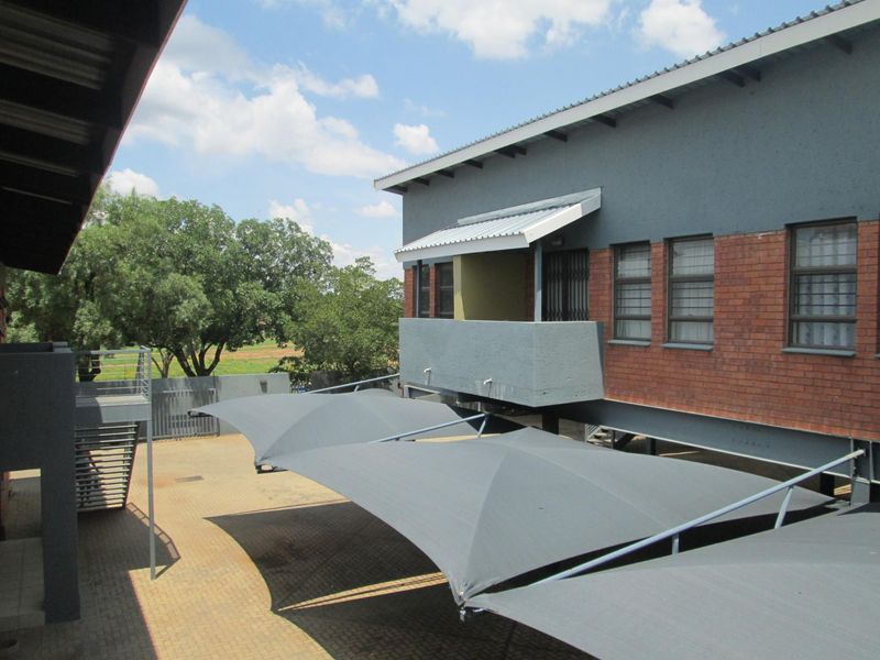 Exterior view of the apartment complex featuring a paved parking area with shade sail carports and a multi-story building with brick and plaster finishes.