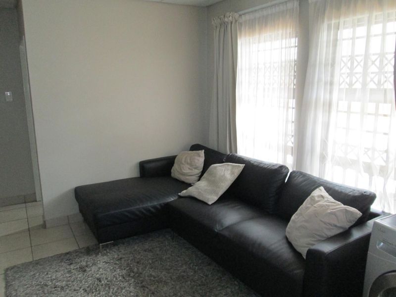 A living room area featuring tiled flooring and large windows fitted with security gates and curtains.