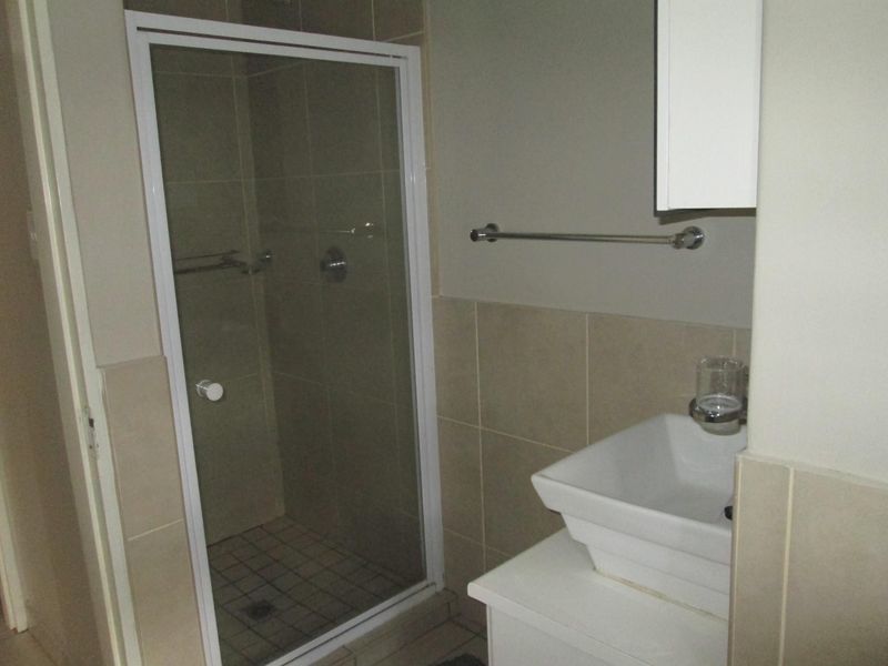 A functional bathroom featuring a glass-enclosed shower, a modern vessel sink with vanity storage, and neutral wall tiling.