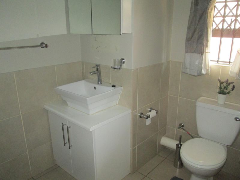 A functional bathroom featuring a modern vessel sink on a vanity cabinet, mirrored medicine cabinet, toilet, and neutral wall and floor tiling.