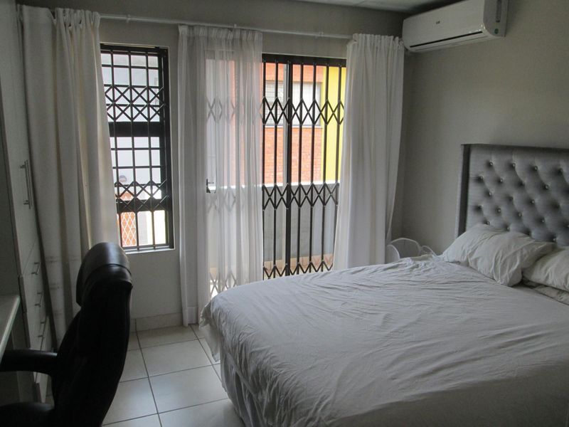 A functional bedroom featuring tiled flooring, a wall-mounted air conditioning unit, and secure access to an external area via security gates.