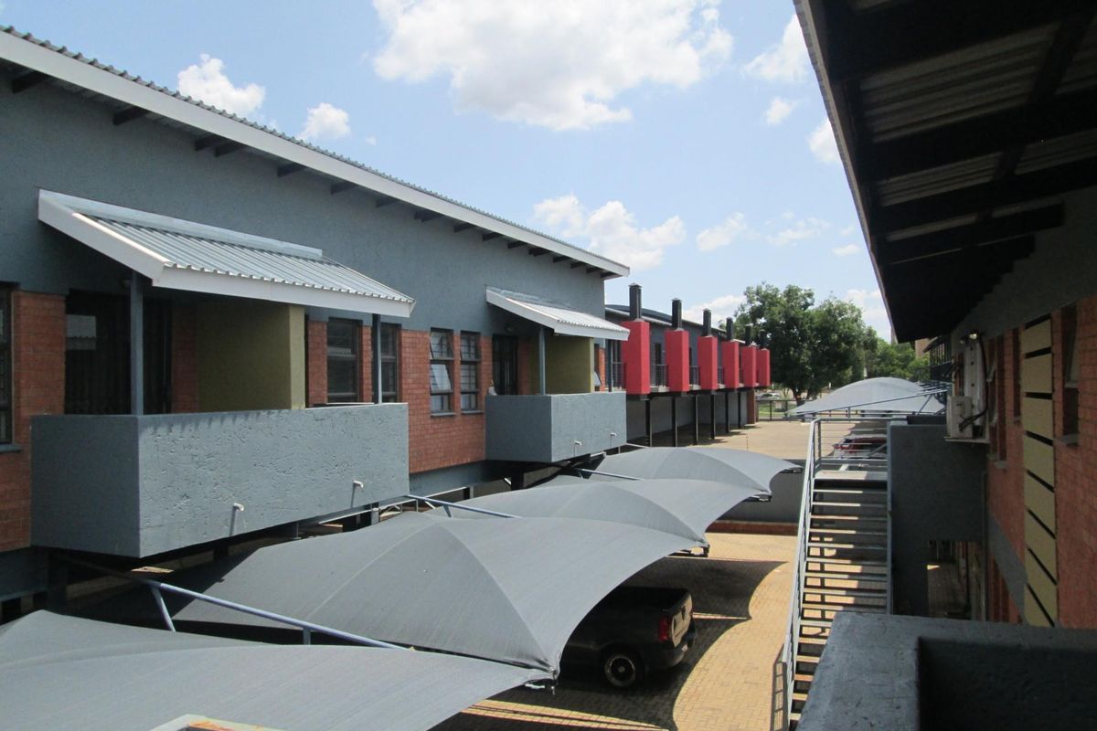 Exterior view of the apartment complex featuring covered parking bays, brick and rendered facades, and external staircases providing access to upper-level units.