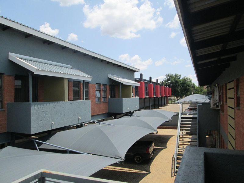 Exterior view of the apartment complex featuring covered parking bays, brick and rendered facades, and external staircases providing access to upper-level units.