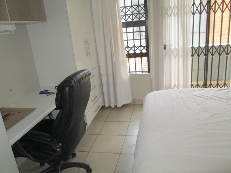 A functional bedroom featuring tiled flooring, built-in cupboards, a built-in desk, and a sliding door with security gate access to the exterior.