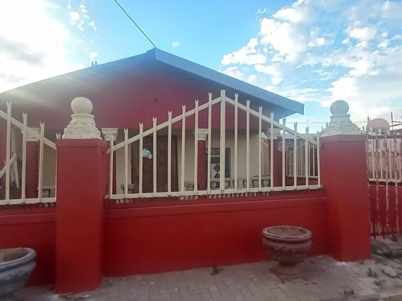 Front view of a residential property featuring a red perimeter wall, metal security fencing, and decorative concrete pillars.