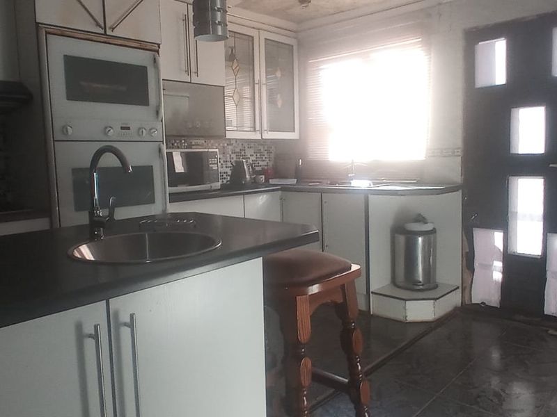 A dated kitchen featuring built-in appliances, tiled backsplash, and fitted cabinetry, requiring cosmetic updates to modernize the space.