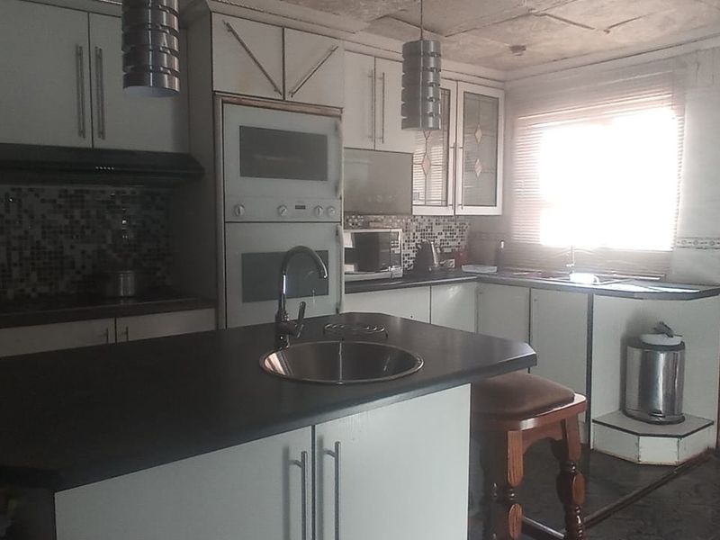 A dated kitchen featuring built-in cabinetry, a central island with a sink, and mosaic tile backsplash, requiring cosmetic updates to improve functionality and aesthetic appeal.