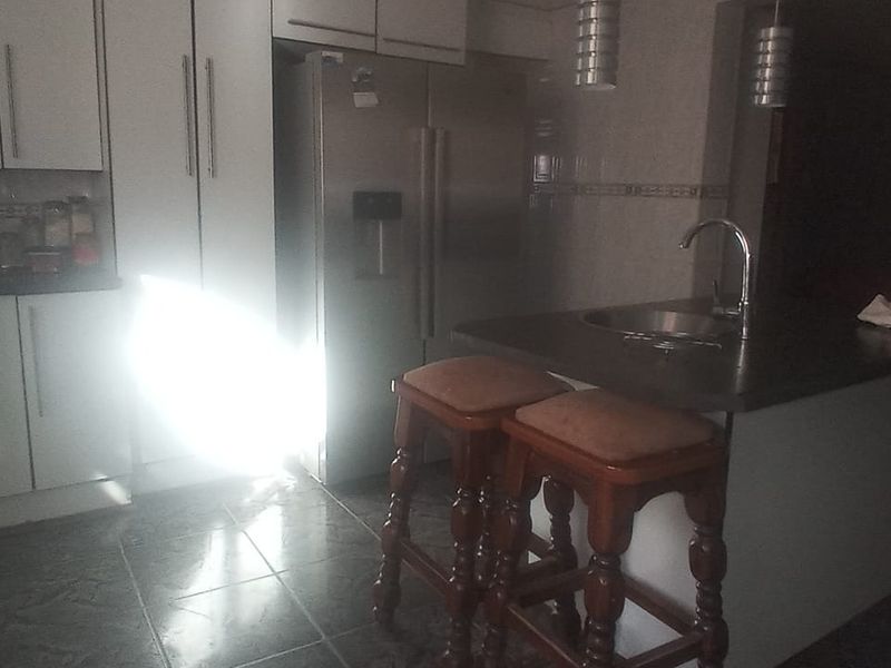 A kitchen featuring built-in cabinetry, a central island with a sink, and tiled flooring, currently showing signs of dated finishes.