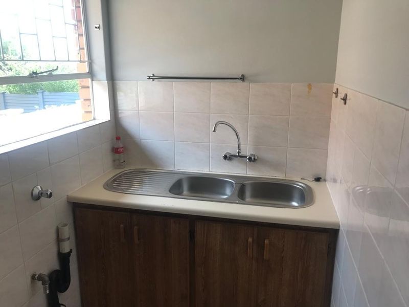 A functional laundry area featuring a double bowl stainless steel sink, tiled splashback, and built-in cabinetry with plumbing connections for appliances.