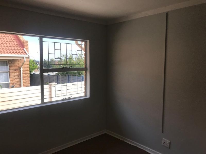 A clean, empty bedroom featuring neutral walls, a window with security bars, and standard electrical fixtures, ready for personalization.