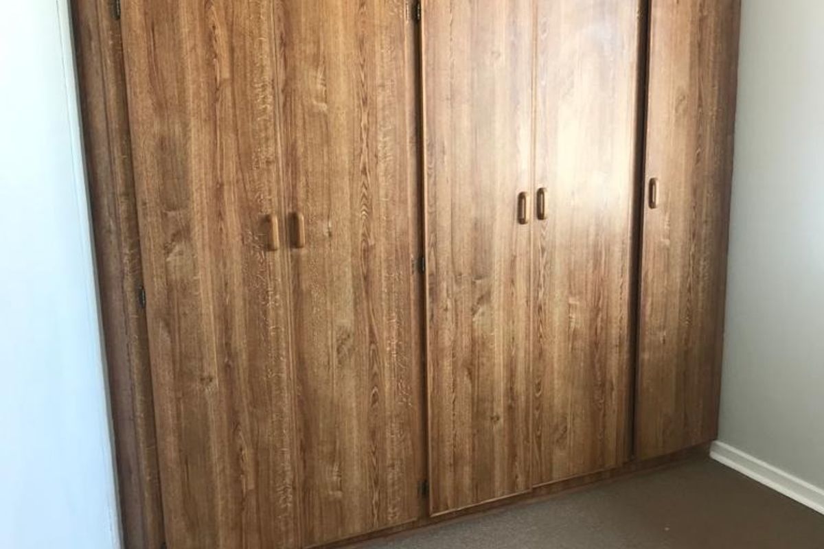 A bedroom featuring floor-to-ceiling built-in wooden cupboards with ample storage space.