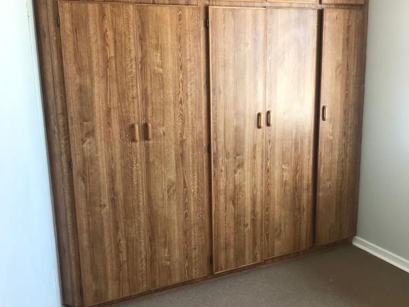 A bedroom featuring floor-to-ceiling built-in wooden cupboards with ample storage space.