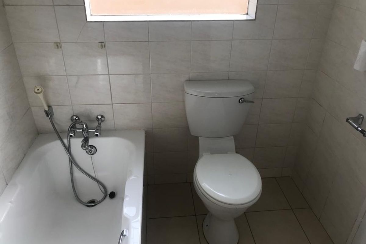 A compact bathroom featuring a standard bathtub with a handheld shower mixer and a white toilet, finished with neutral ceramic wall and floor tiles.