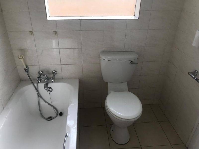 A compact bathroom featuring a standard bathtub with a handheld shower mixer and a white toilet, finished with neutral ceramic wall and floor tiles.