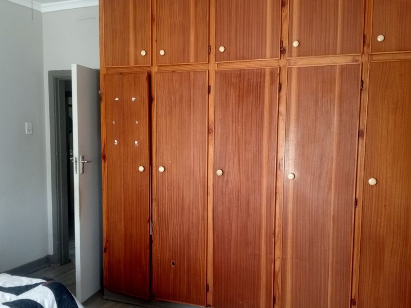 Bedroom featuring extensive floor-to-ceiling built-in wooden cupboards with some visible wear and missing hardware.