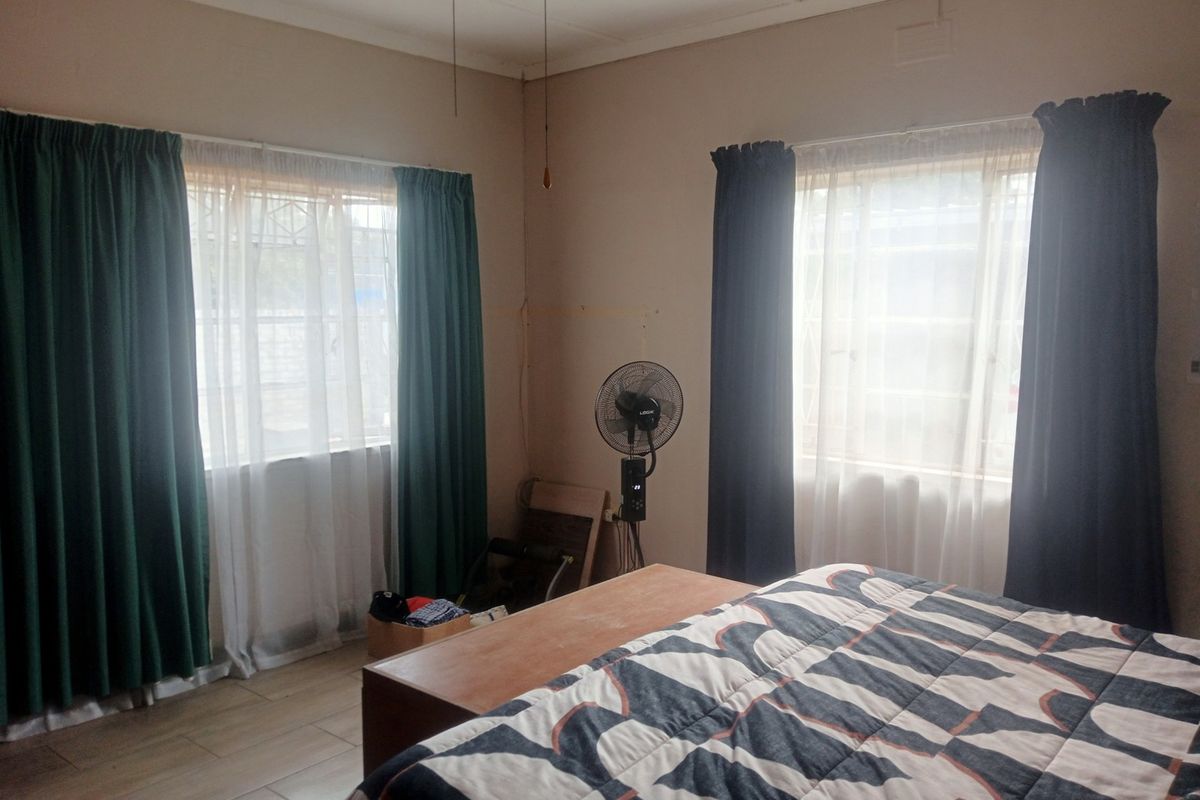 A bedroom featuring tiled flooring, dual windows with security bars, and a ceiling fan, offering a functional and well-lit living space.