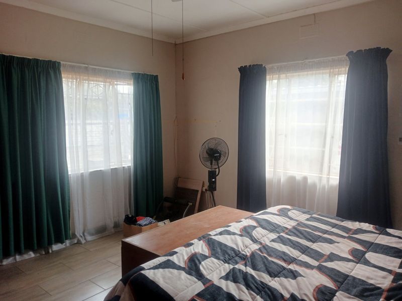 A bedroom featuring tiled flooring, dual windows with security bars, and a ceiling fan, offering a functional and well-lit living space.