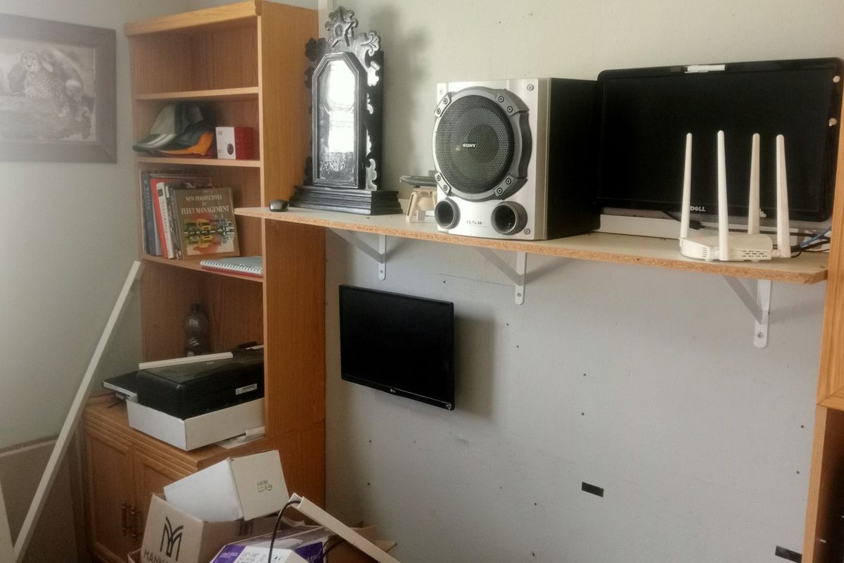 A living area featuring built-in wooden cabinetry and wall-mounted shelving units, currently showing signs of wear and requiring cosmetic updates.