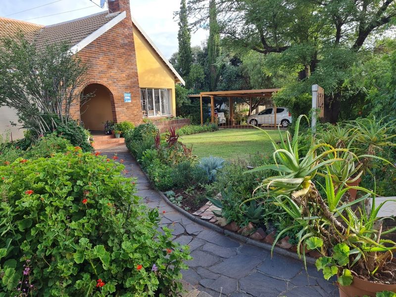 Front view of a charming brick house featuring an arched entrance, a stone-paved walkway, a well-maintained garden, and a covered carport.