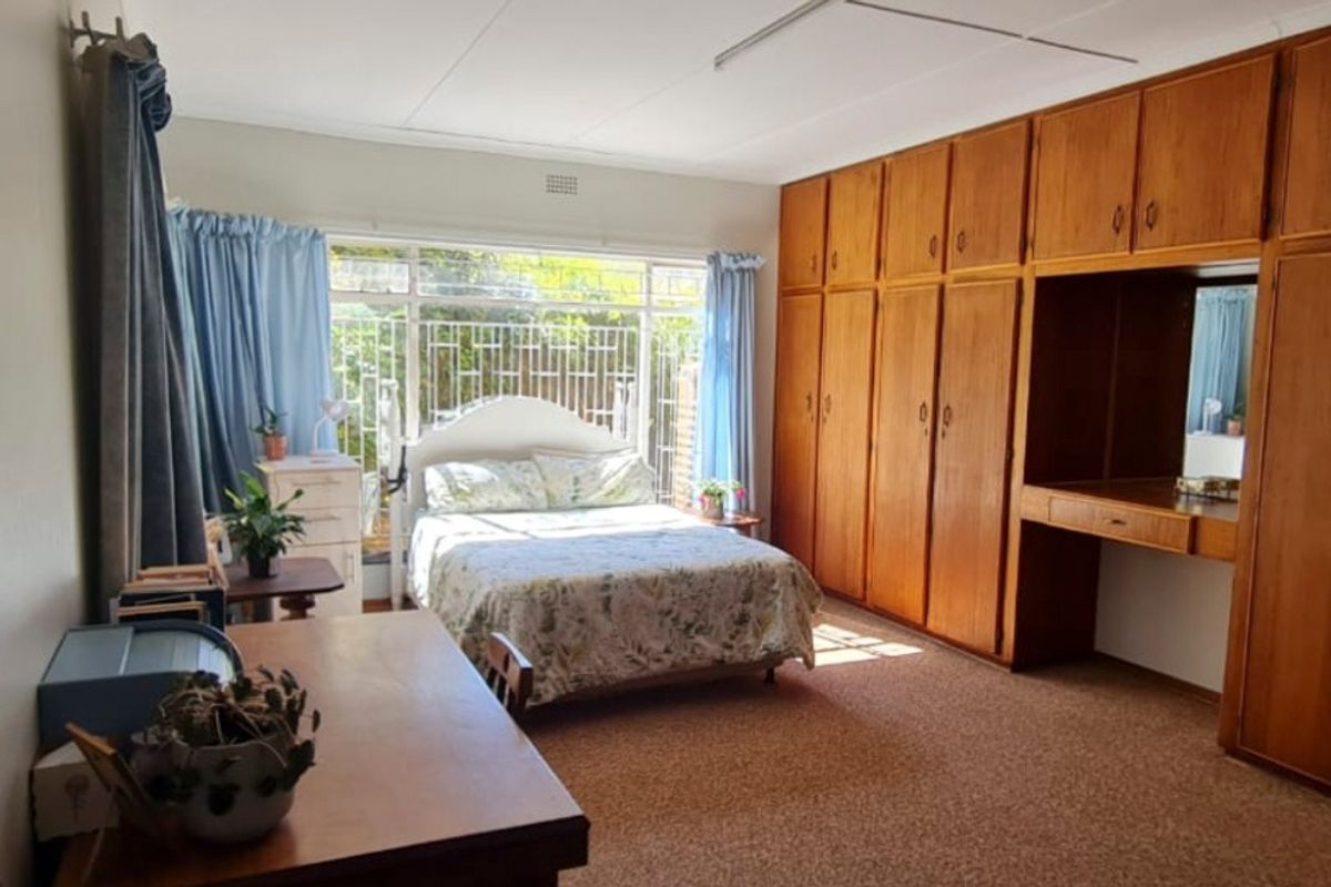 Spacious bedroom featuring extensive built-in wooden cabinetry with an integrated vanity, large windows with security bars, and carpeted flooring.