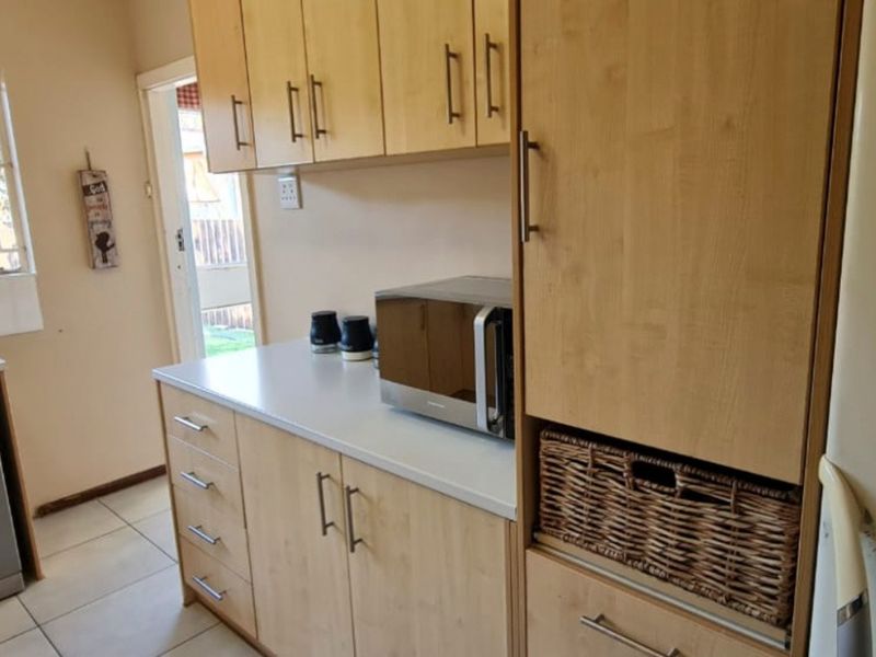 A functional kitchen featuring light wood-toned cabinetry, laminate countertops, tiled flooring, and space for integrated appliances with direct access to the exterior.